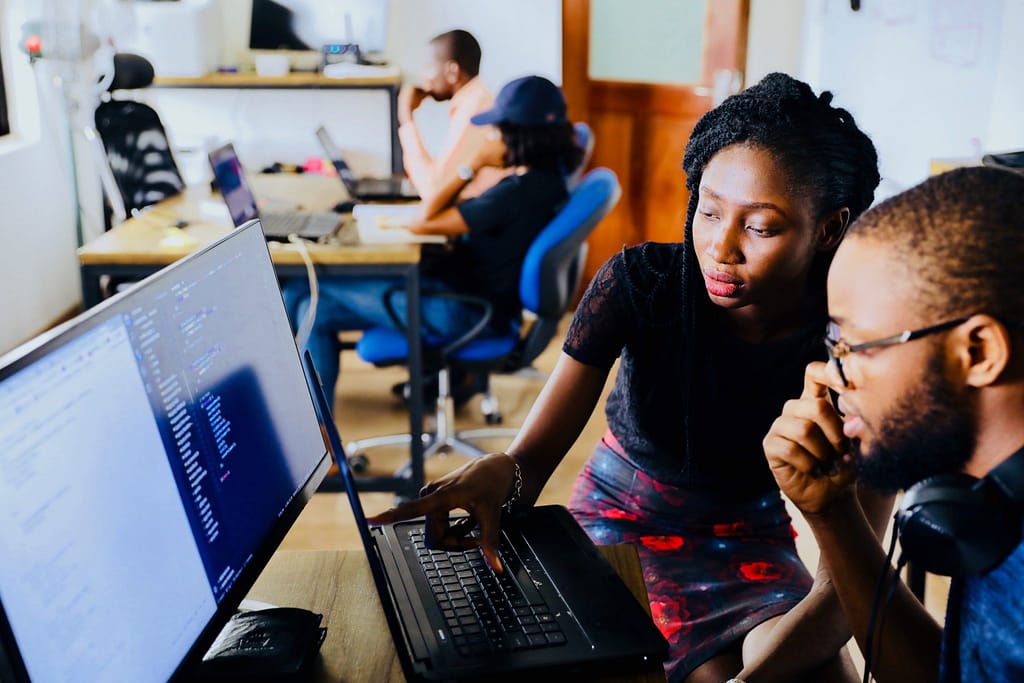 A young working woman point at something on a laptop to a young man