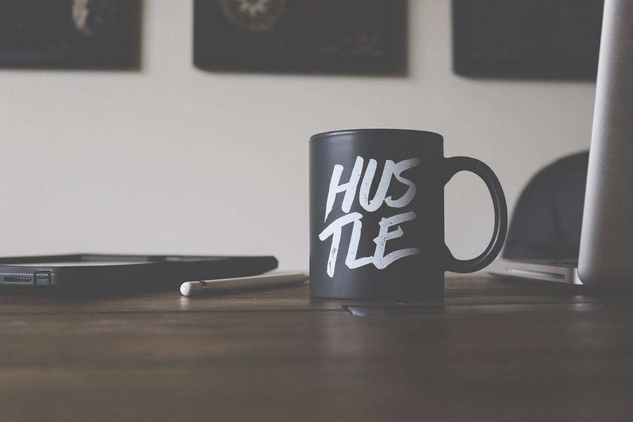 A coffee mug with hustle written on it next to a laptop and pad
